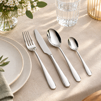 24-piece stainless steel cutlery set with a fork, knife, soup spoon, and teaspoon arranged on a beige linen tablecloth next to a white plate, with a glass of water and flowers in the background.