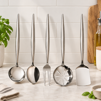 Five stainless steel kitchen utensils with long handles are arranged upright on a white marble countertop against a white subway tile backsplash. The utensils include a ladle, a spoon, a fork, a slotted serving spoon, and a spatula.