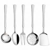 Five stainless steel kitchen utensils with long handles are arranged on a light marble countertop in a bright kitchen setting. The utensils include a ladle, spoon, fork, slotted spoon, and spatula.