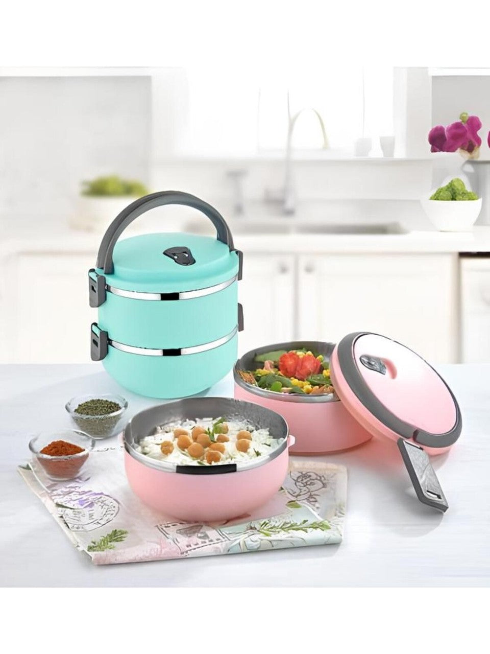 A mint green stackable lunch box with three tiers and a dark gray lid, set on a marble countertop