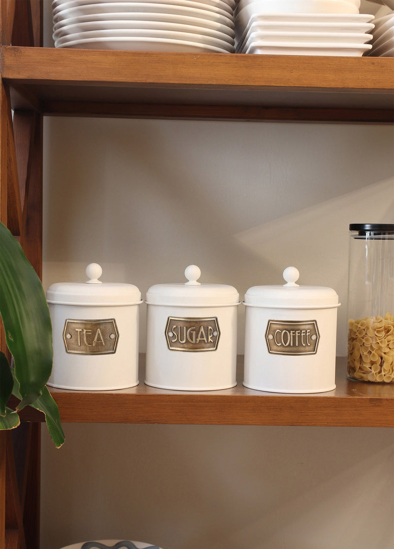 A set of three white cylindrical canisters with lids, each labeled with different names: Tea, Coffee, and Sugar.