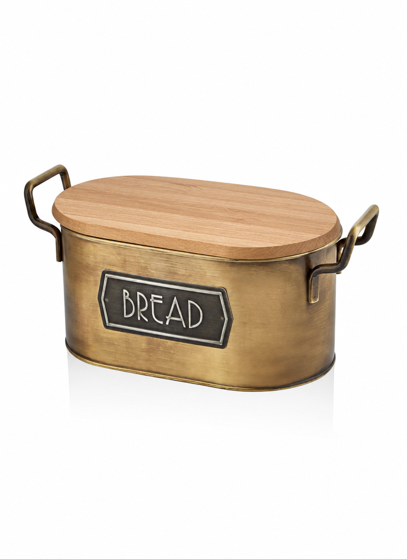 An oval-shaped bread storage container with a brushed brass metal body, a light wood lid, and dark metal side handles. A black label on the front reads 'BREAD' in white lettering.