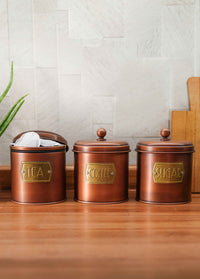 A set of three copper-colored galvanised steel canisters with labels Coffee, Sugar, and Tea on them, designed for storing coffee, tea, and sugar.