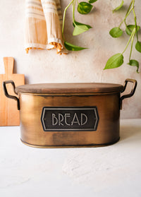 A gold bread bin made from galvanised steel with a wooden lid, hand-painted details, and labeled 'BREAD' on the front.
