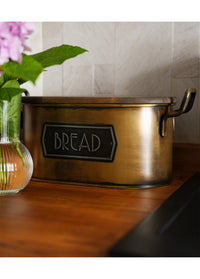 A gold bread bin made from galvanised steel with a wooden lid, hand-painted details, and labeled 'BREAD' on the front.
