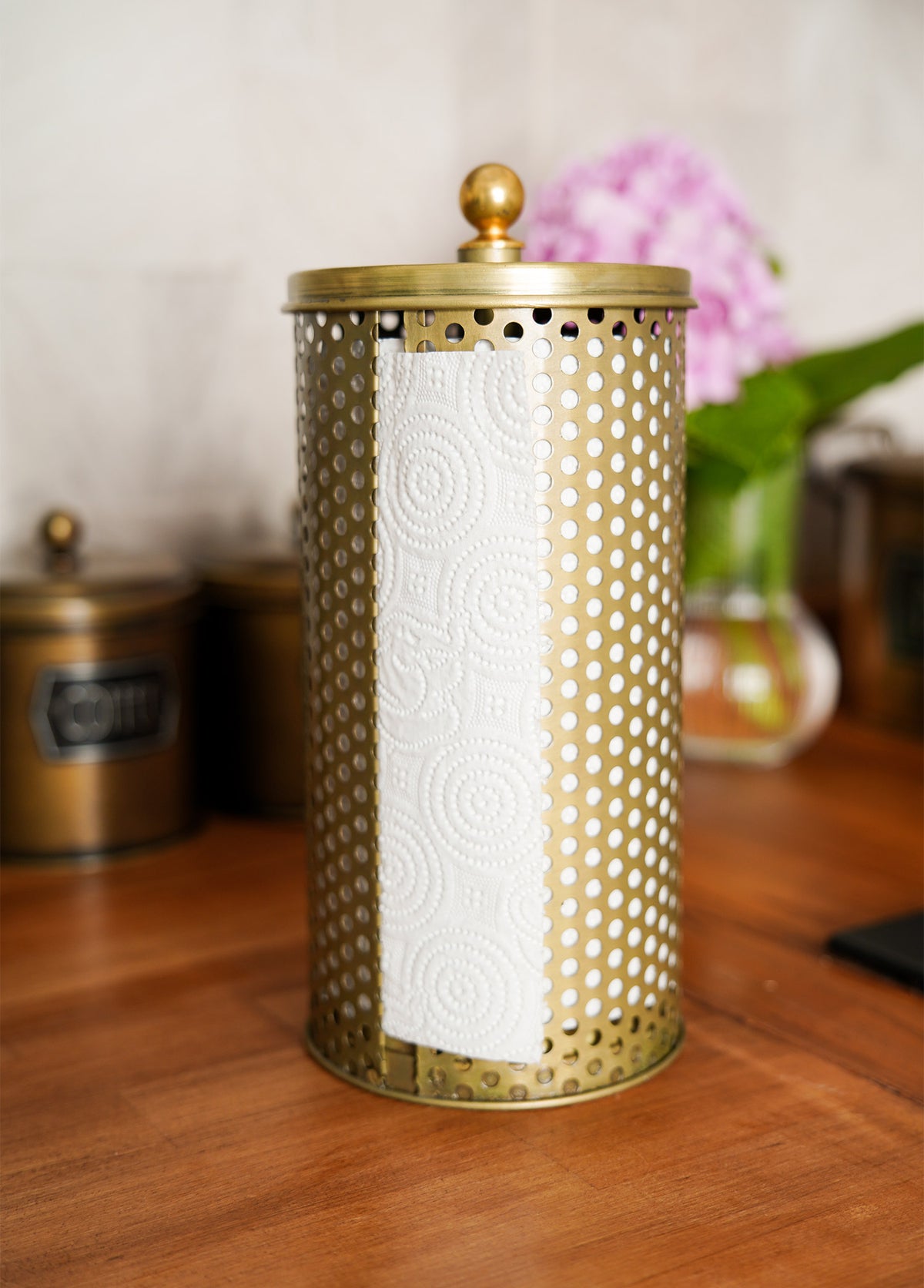 A gold paper towel holder made from galvanised steel with a paper towel roll partially inserted.